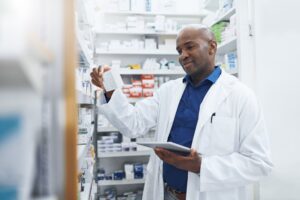 Pharmacist reviewing inventory on a shelf, illustrating strategies for pharmacy overhead reduction by optimizing inventory and procurement management.