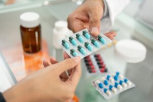 A pharmacist hands a blister pack of capsules to a customer over the counter, representing prescription fulfillment and efficient pharmacy operation refresh.